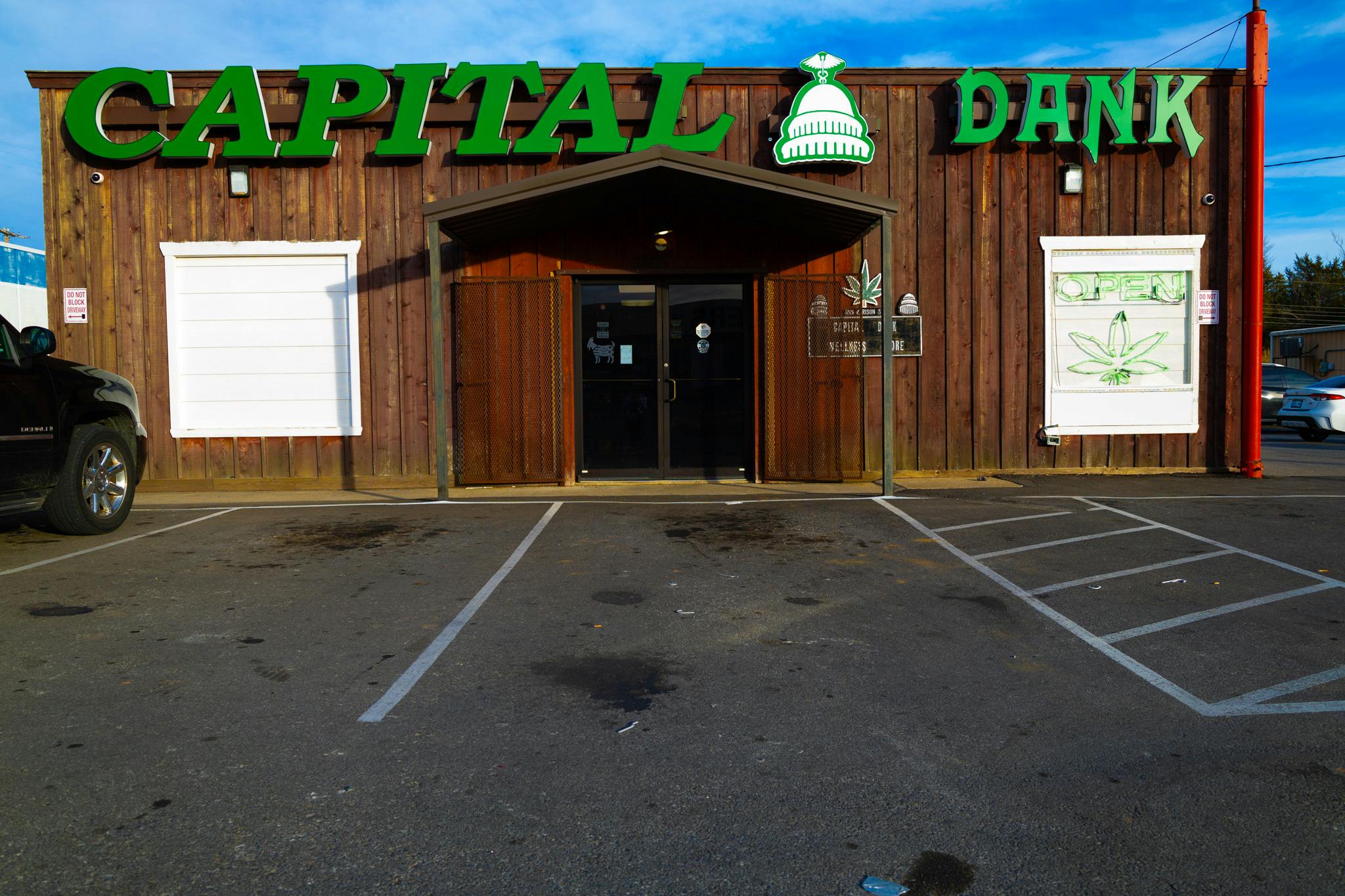 Exterior of Capital Dank dispensary in Shawnee, Oklahoma, with wooden storefront, green signage, and visible parking in front of the entrance.