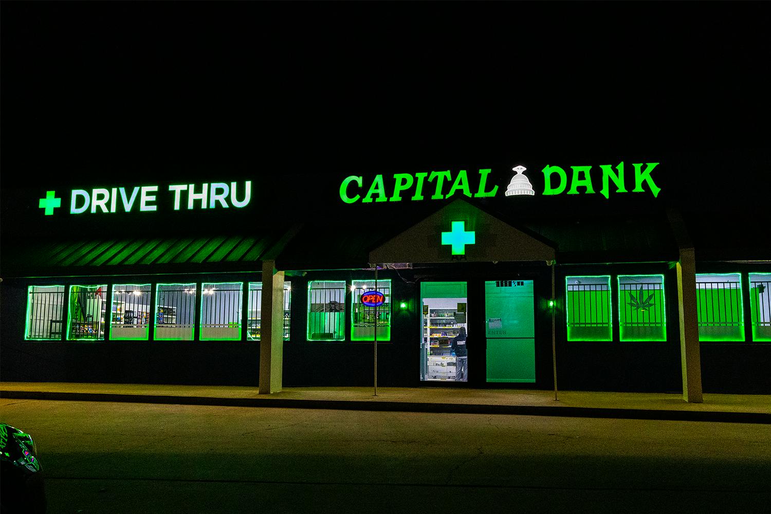 Capital Dank dispensary in Tulsa, Oklahoma, at night with green neon signage and a drive-thru entrance highlighted above the storefront.